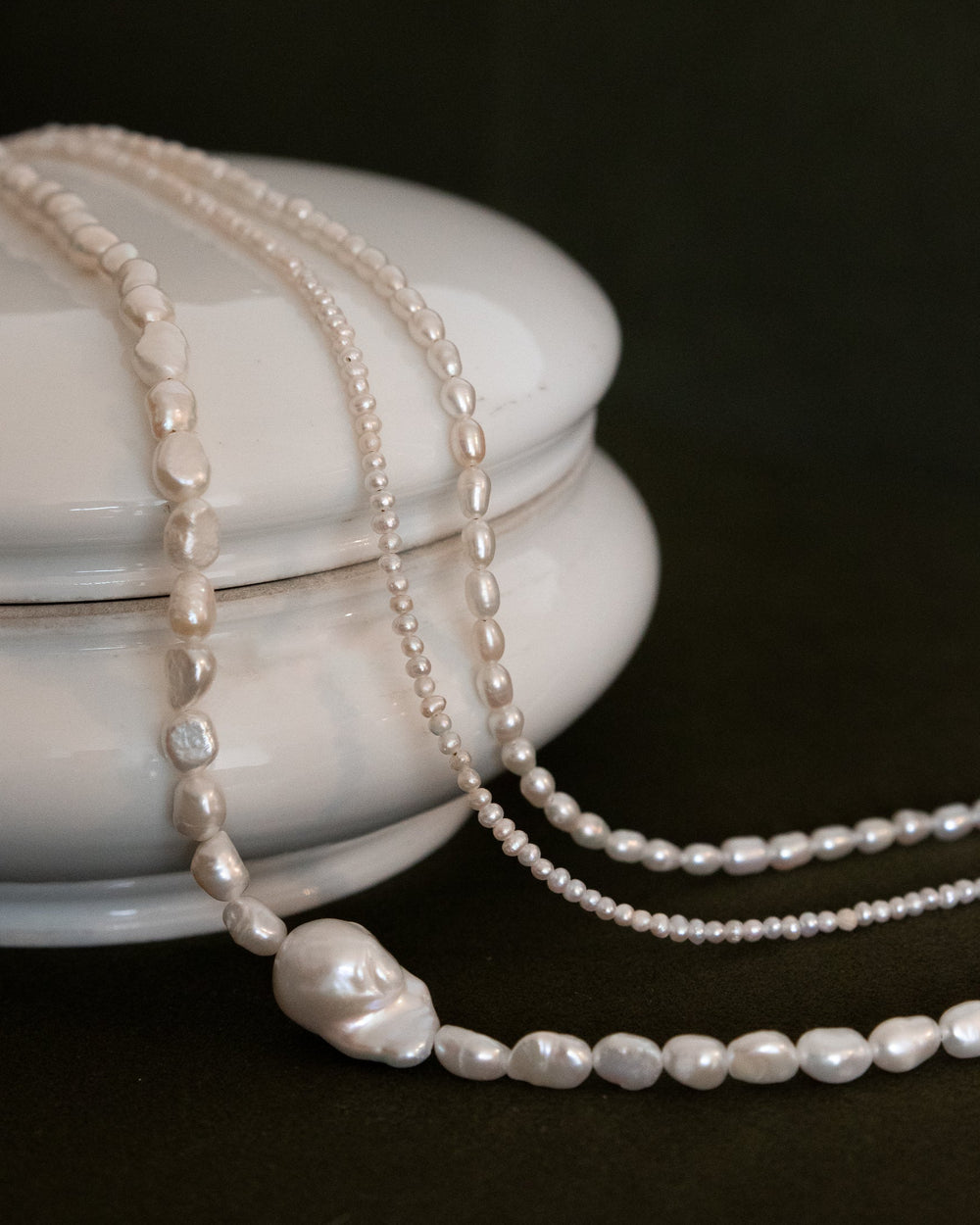 Pearl necklace draped over a white ceramic container on a dark background