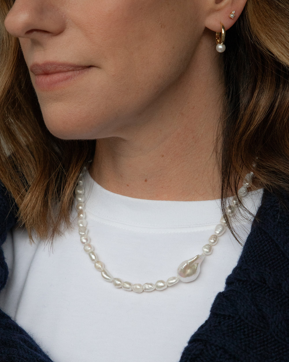 Close-up of a person wearing a pearl necklace and earrings.