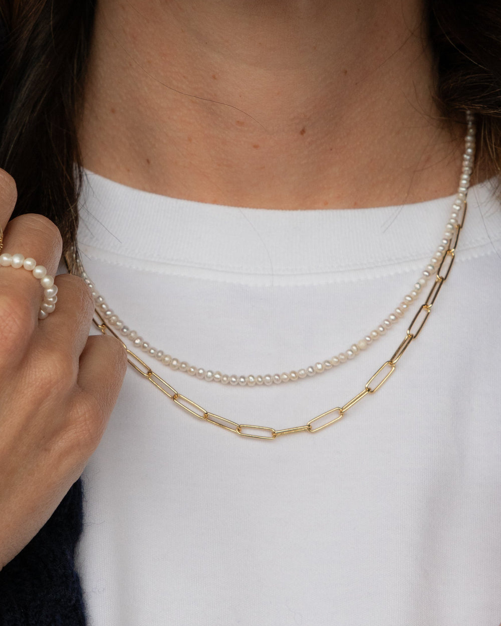 Close-up of a person wearing pearl and gold necklaces with a white shirt.